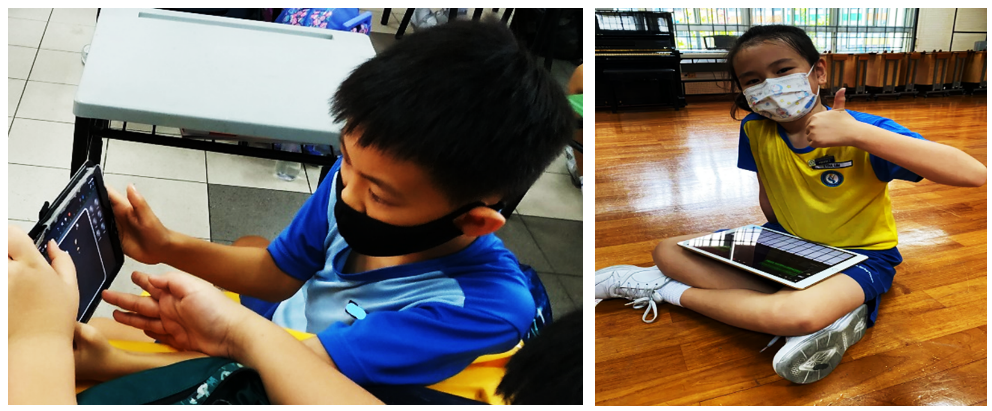 Two masked children in blue uniforms use tablets; one sits cross-legged giving a thumbs up.
